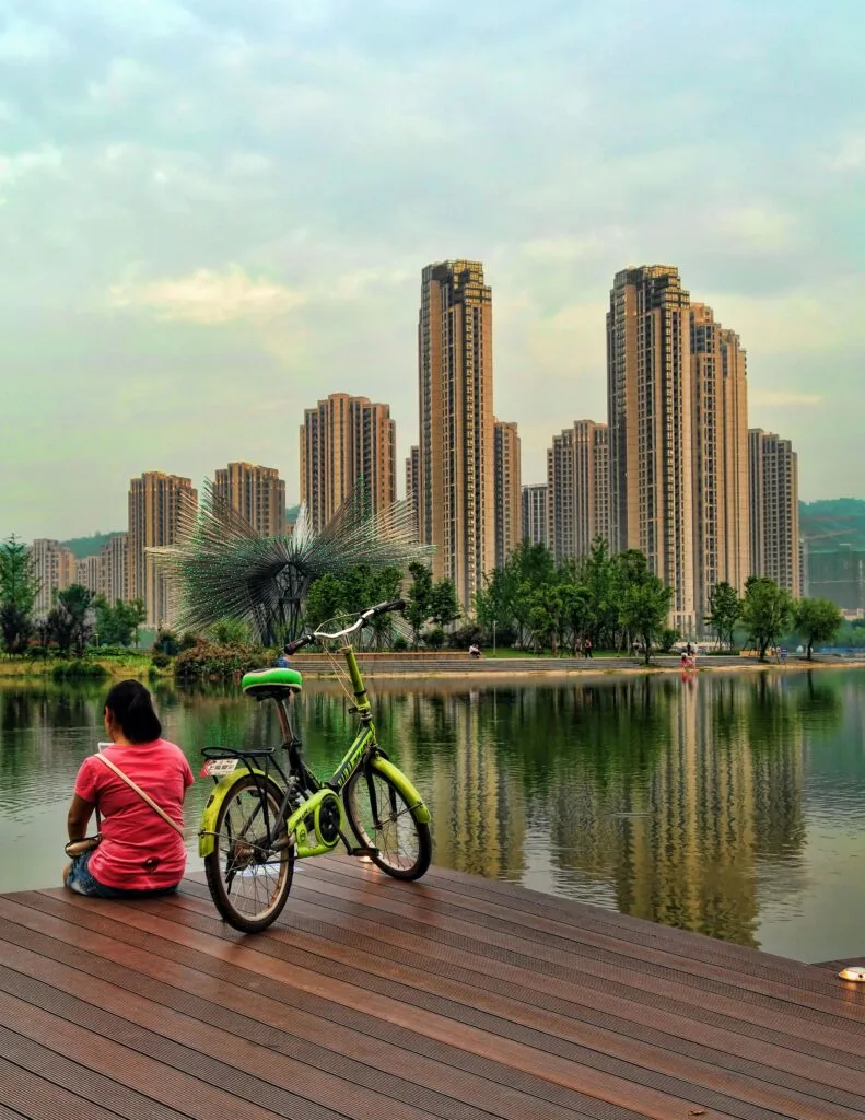 A serene scene in Changsha featuring a woman sitting by a lake with skyscrapers in the background.