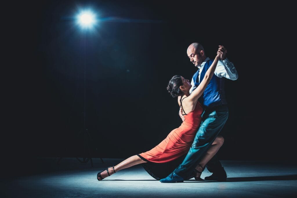 Elegant couple performing tango under a dramatic spotlight, showcasing passion and grace.show de tango Buenos Aires escenario