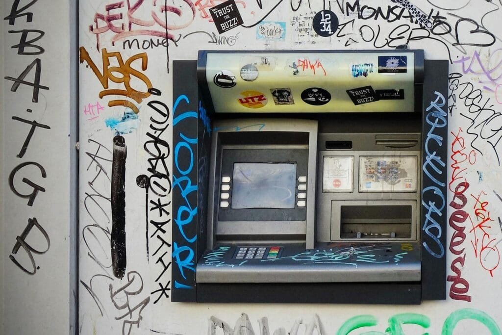 An ATM embedded in a graffiti-covered wall, showcasing vibrant street art in a city setting.¿Es seguro ocupar el ATM en Sudamerica?