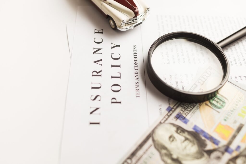 Close-up image of an insurance policy with a magnifying glass, money, and toy car.Poliza de seguro para mochileros